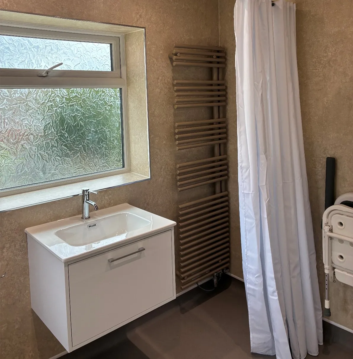 Completed mobility bathroom in Leeds featuring a level access shower with white curtain, wall-mounted vanity unit and heated towel rail.