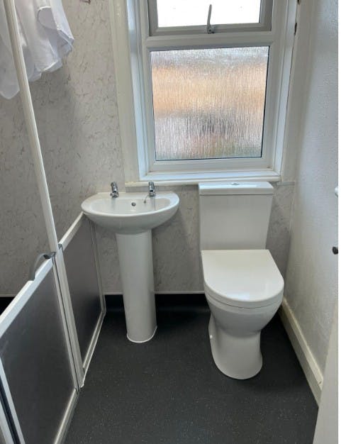 Raised-height WC and pedestal basin fitted as part of an accessible disabled bathroom adaptation with contrasting Altro Aquarius flooring.