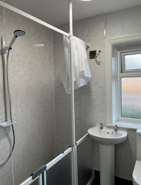 Accessible disabled wet room in Huddersfield featuring half-height shower screens, white marble wall panels, pedestal basin and level-access shower installed by More Ability.