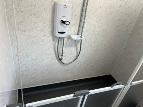 Mira ATL Flex thermostatic shower unit installed in a disabled wet room adaptation with dark slip-resistant vinyl flooring and white marble effect wall panels.