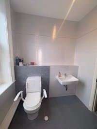 Fully refurbished accessible bathroom showing Closomat wash and dry WC, wall-hung basin and coordinated grey wall boards with off-white tiled walls.